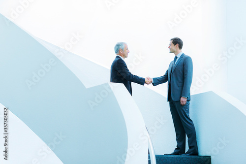 Businessmen shaking hands on staircase of office building photo