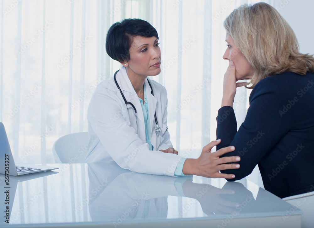 Female doctor consoling sad woman at desk in office Female doctor consoling sad woman at desk in office