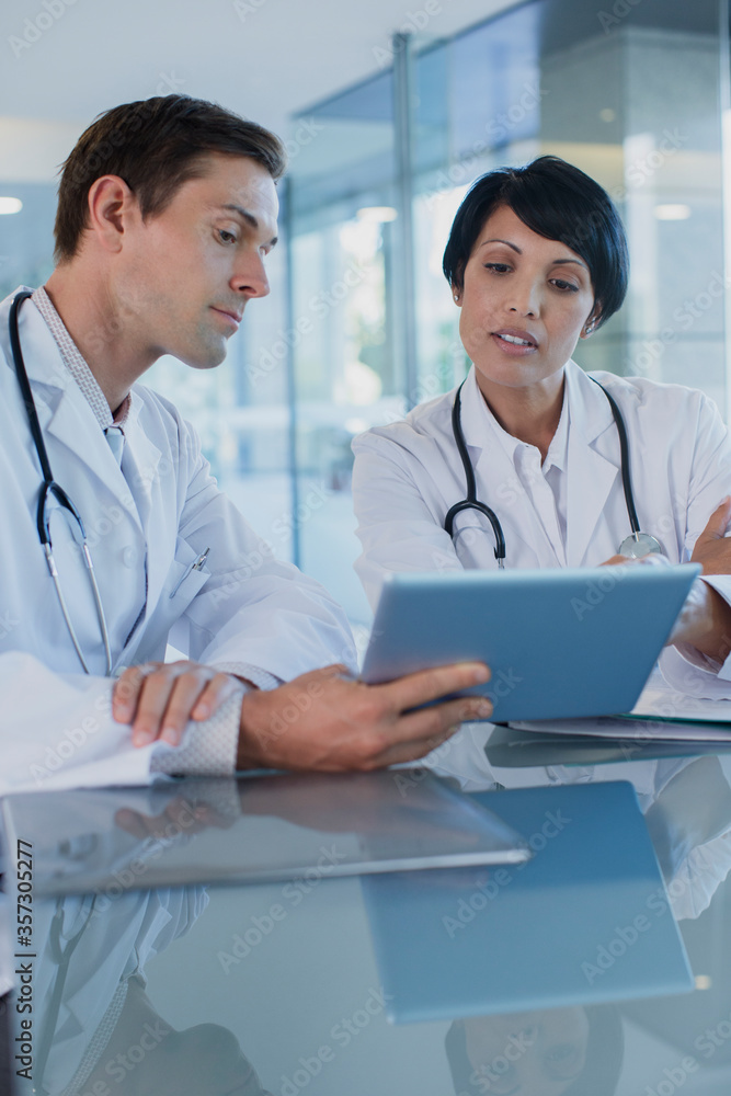 Doctors discussing patient's treatment at desk, using digital tablet Doctors discussing patient's treatment at desk, using digital tablet