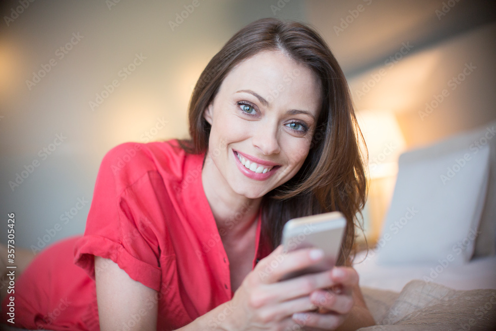 Portrait smiling woman wearing red dress lying on bed smart phone Portrait smiling woman wearing red dress lying on bed smart phone