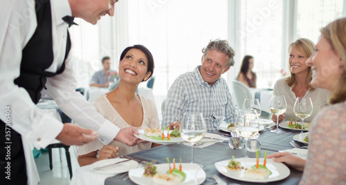 Waiter serving fancy dish to woman sitting at restaurant table