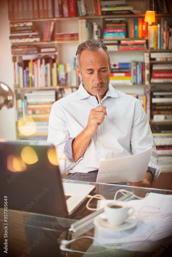 Businessman reading paperwork at home office desk