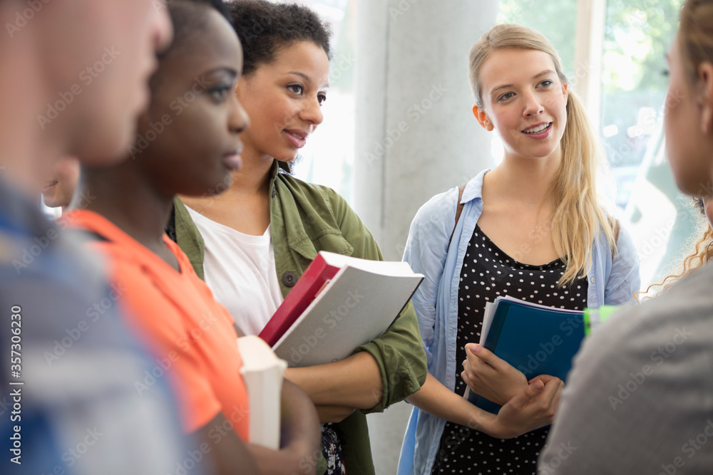 University students with books standing in corridor talking