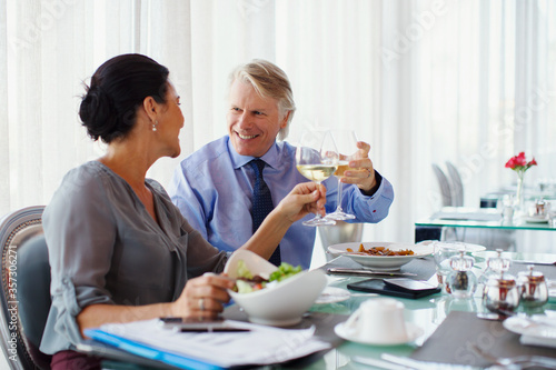 Smiling mature couple raising toast white wine at restaurant table