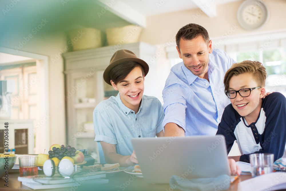 Mid adult man with teenage boys using laptop in kitchen