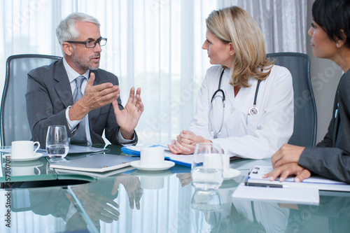 Female doctor, man and woman talking at table in conference room
