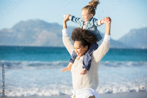 Mother carrying daughter on her shoulders on beach