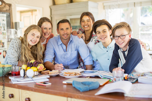 Group of teenagers with mid adult man sitting at table in dining room