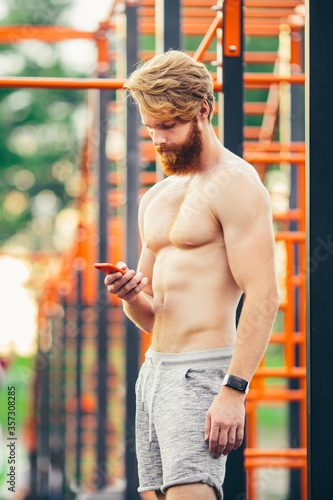 athlete looking smart phone. On wrist with smart watch. Sportsman checking performances after training. Fitness, sport, lifestyle concept. man using fitness app. Portrait guy in gym resting workout © Elizaveta