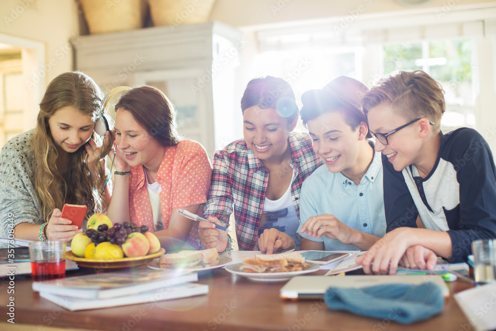 Group of teenagers using electronic devices at table in dining room Group of teenagers using electronic devices at table in dining room