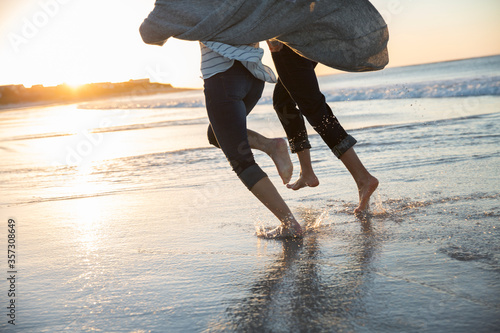 Legs of young couple running on beach at sunset