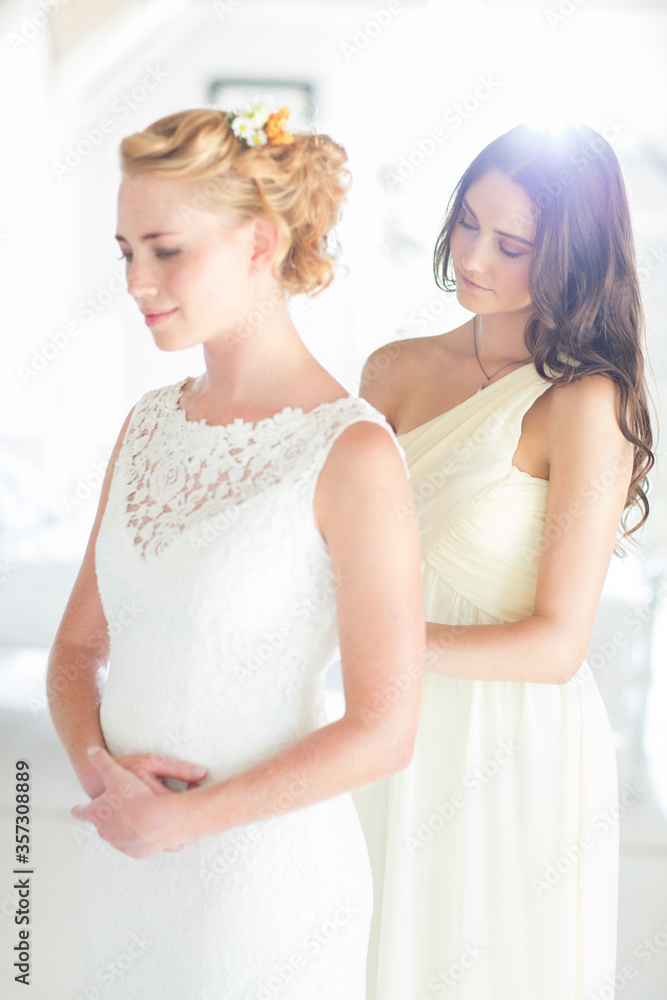 Bridesmaid helping bride with dressing in bedroom Bridesmaid helping bride with dressing in bedroom