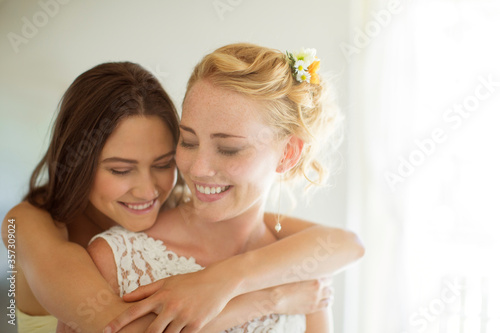Bridesmaid embracing bride in bedroom