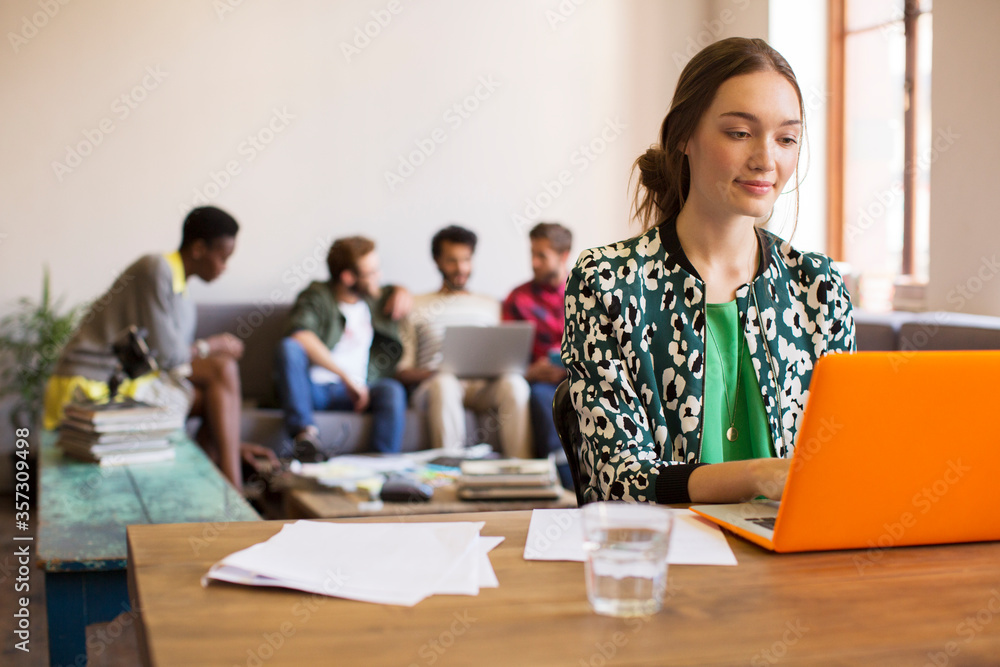 Creative businesswoman working at laptop with paperwork in office Creative businesswoman working at laptop with paperwork in office