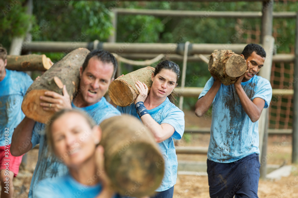 Fototapeta premium Determined team carrying logs on boot camp race course