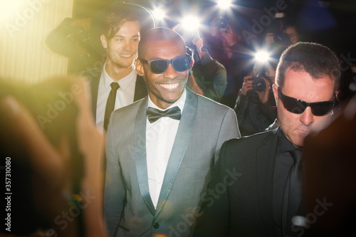 Smiling celebrity in sunglasses being photographed by paparazzi photographers at event photo