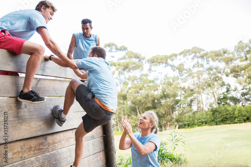 Teammates helping man over wall on boot camp obstacle course photo