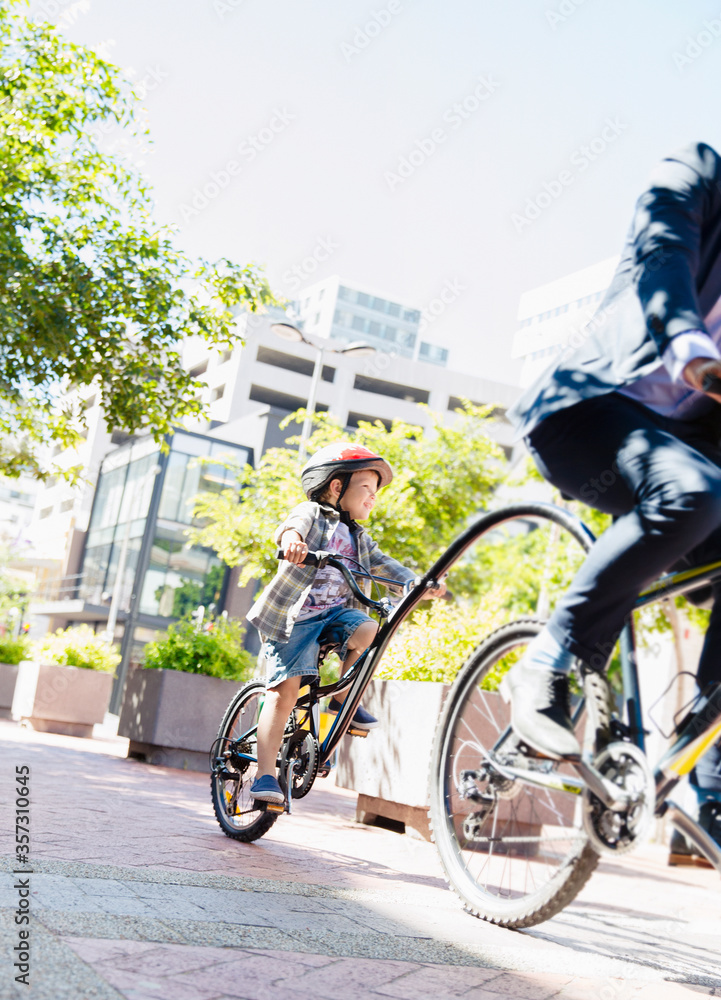 Son in helmet riding tandem bicycle businessman father in sunny urban park