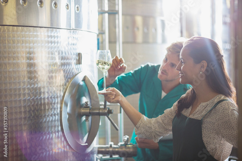 Vintners examining white wine at stainless steel vat in winery cellar