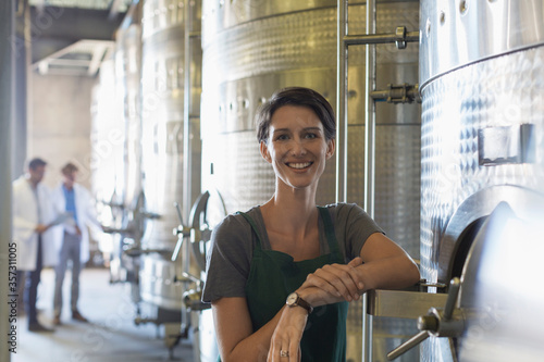 Portrait smiling vintner at stainless steel vat in winery cellar photo