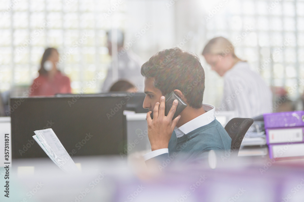 Fototapeta premium Businessman with paperwork talking on cell phone in office