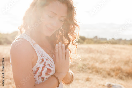 Serene boho woman with hands at heart center in sunny rural field photo