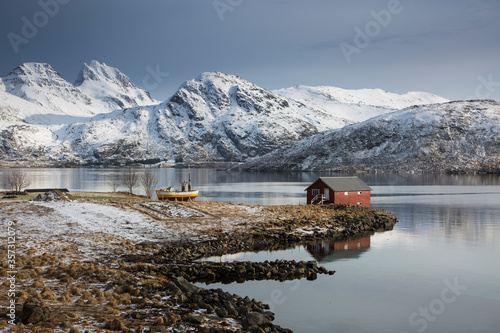 Fotografia, Obraz Fishing hut on cold bay below snow covered mountains, Norway
