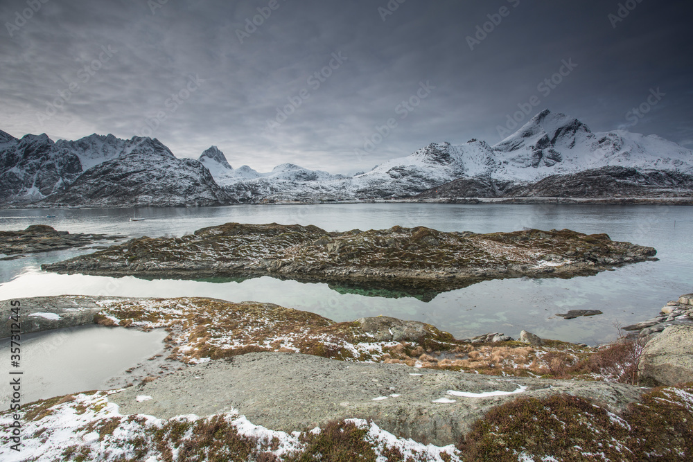 Snow covered mountain range behind craggy bay, Sund, Lofoten Islands, Norway Snow covered mountain range behind craggy bay, Sund, Lofoten Islands, Norway