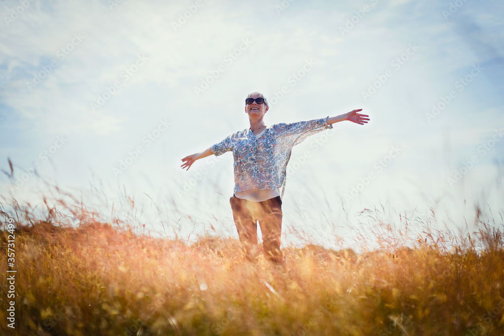 Fototapeta premium Carefree senior woman running with arms outstretched in sunny field
