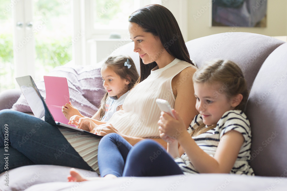 Mother daughters with laptop, cell phone digital tablet on sofa Mother daughters with laptop, cell phone digital tablet on sofa