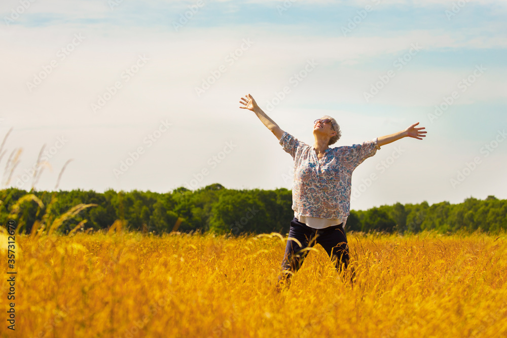 Exuberant senior woman with arms outstretched in sunny rural field Exuberant senior woman with arms outstretched in sunny rural field