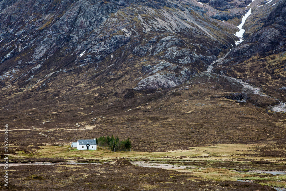 House in remote valley below craggy mountains, Glencoe, Scotland