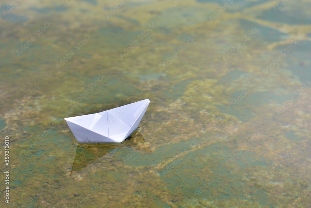 Barco de papel flotando sobre el agua de un estanque