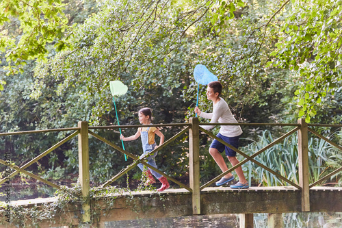 Brother and sister running with butterfly nets on footbridge in park