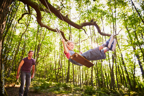 Father pushing daughter on rope swing in forest photo