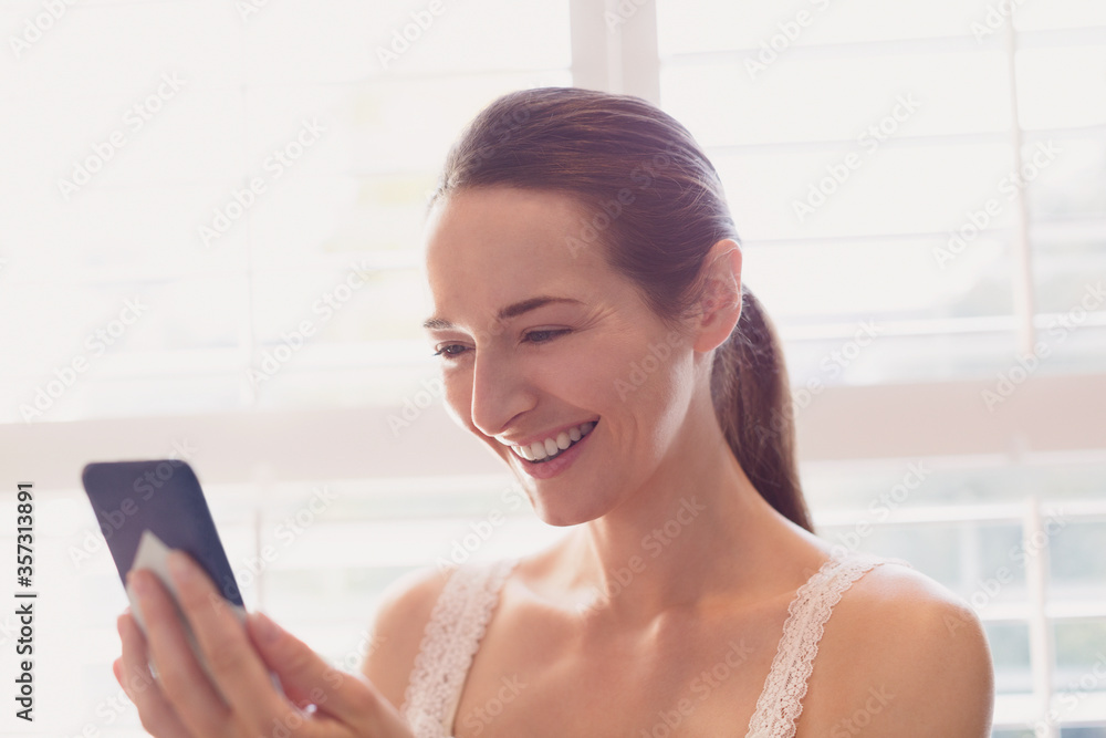 Smiling woman texting with cell phone at window Smiling woman texting with cell phone at window