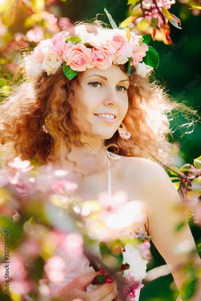 Beauty young happy woman in a flowered garden. Girl among the flowers of apple trees, cherries. Springtime scene. Positive model with a wreath on her hair. Lifestyle Beauty young happy woman in a flowered garden. Girl among the flowers of apple trees, cherries. Springtime scene. Positive model with a wreath on her hair. Lifestyle