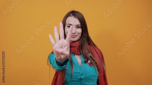 Showing four 4 fingers hand gesture, show the number three with hands, pointing up arm while smiling confident, happy. Young attractive woman with brown hair and eyes, decoration on blue shirt