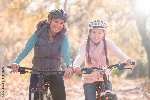 Portrait of smiling mother and daughter on mountain bikes in woods