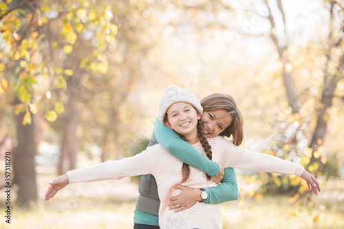 Portrait mother hugging daughter with arms outstretched among autumn leaves