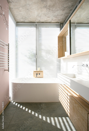 Light through blinds behind soaking tub in modern bathroom