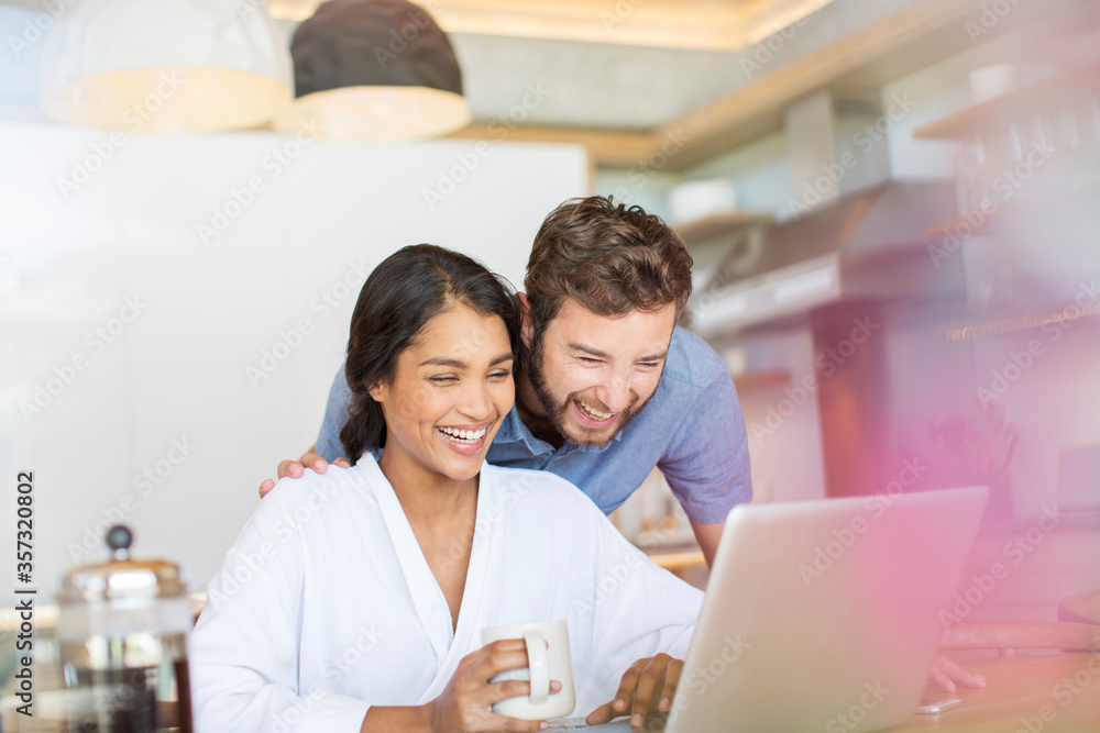 Laughing couple drinking coffee and using laptop Laughing couple drinking coffee and using laptop
