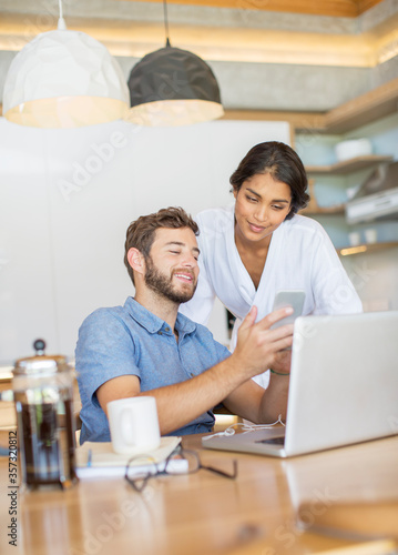 Couple texting with cell phone at laptop