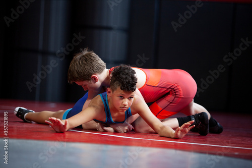 Wrestlers in red and blue singlets practicing on a red mat. 