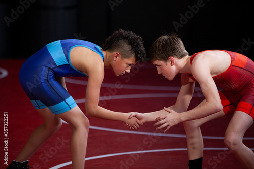 Wrestlers in red and blue singlets practicing on a red mat. 