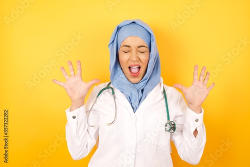 Emotive Caucasian doctor man laughs loudly, hears funny joke or story, raises palms with satisfaction, dressed in medical uniform, being overjoyed over yellow background. People and emotions concept.