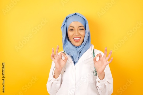 Chill everything is perfect. Portrait of happy and delighted doctor woman wearing medical uniform and hiyab recommending good quality product showing ok gesture and smiling satisfied.