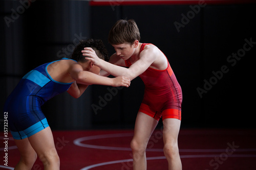 Wrestlers in red and blue singlets practicing on a red mat. 