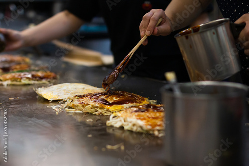 Fototapeta Hand spreading an Okonomiyaki sweet savory sauce at the top