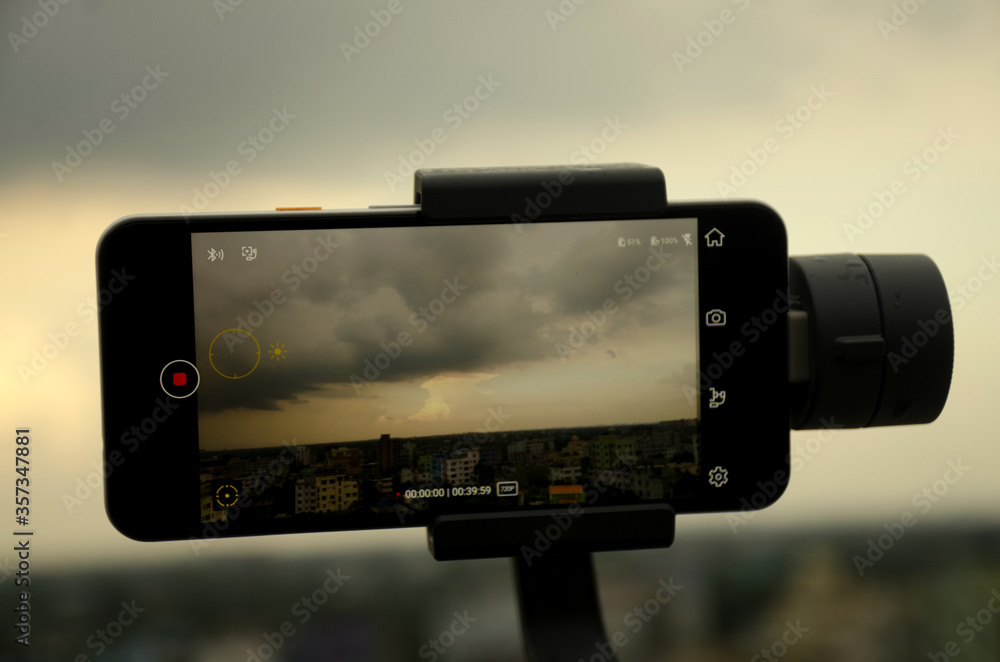 Savar, Dhaka, Bangladesh-June 5, 2020:  Mobile phone Google pixel 3A is shooting a video using gimbal dramatic sky with clouds background is bokeh in the afternoon after raining Video filming concept.